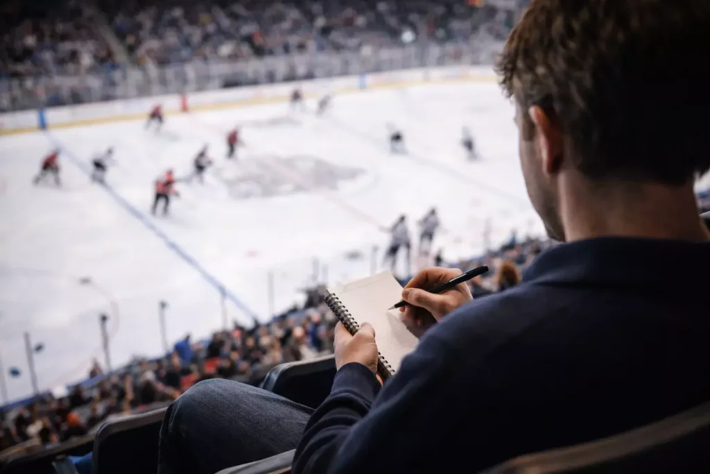 Persoon die een ijshockeywedstrijd analyseert met notitieblok in de hand